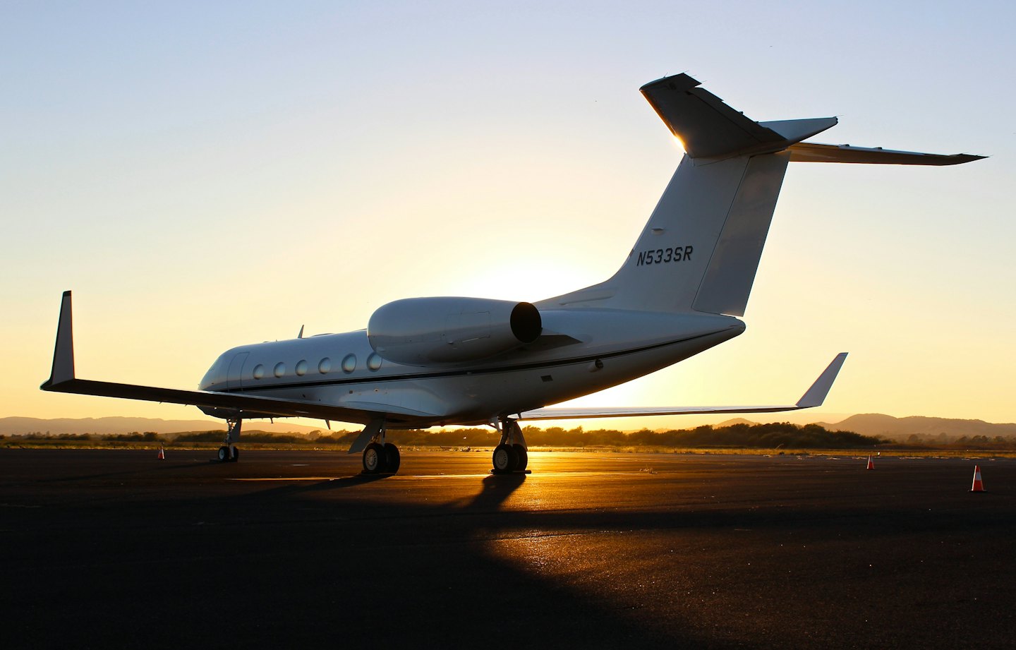 Een witte privéjet staat bij zonsondergang op een asfaltbaan.